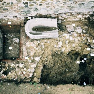 Obr. 49: Veveří - hrad 2000. Sondáž pro SHP. Sonda č. 1. Odkrytá archeologická situace v sondě zachycuje zalomené základy středověkého kamenného zdiva zaniklého paláce se zbytkem ostění interiérové branky při V stěně sondy. V SZ části je zdivo porušené novověkou cihlami vyzděnou odpadní jámou u níž se nacházelo tzv. kamenné zrcadlo původně umístěné v boxech koníren – pohled od SZ (foto P. Vitula).