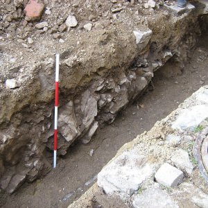 Obr. 138: Veveří – hrad 2017/01. Kanalizace. Vystupující skalní podloží pokryté  tenkou středověkou vrstvou (15. stol.) v profilu výkopu pro kanalizaci před vstupem do anglického traktu od JV z nádvoří pod věžemi hranolovou a prachovou – pohled od JV (foto P. Vitula).